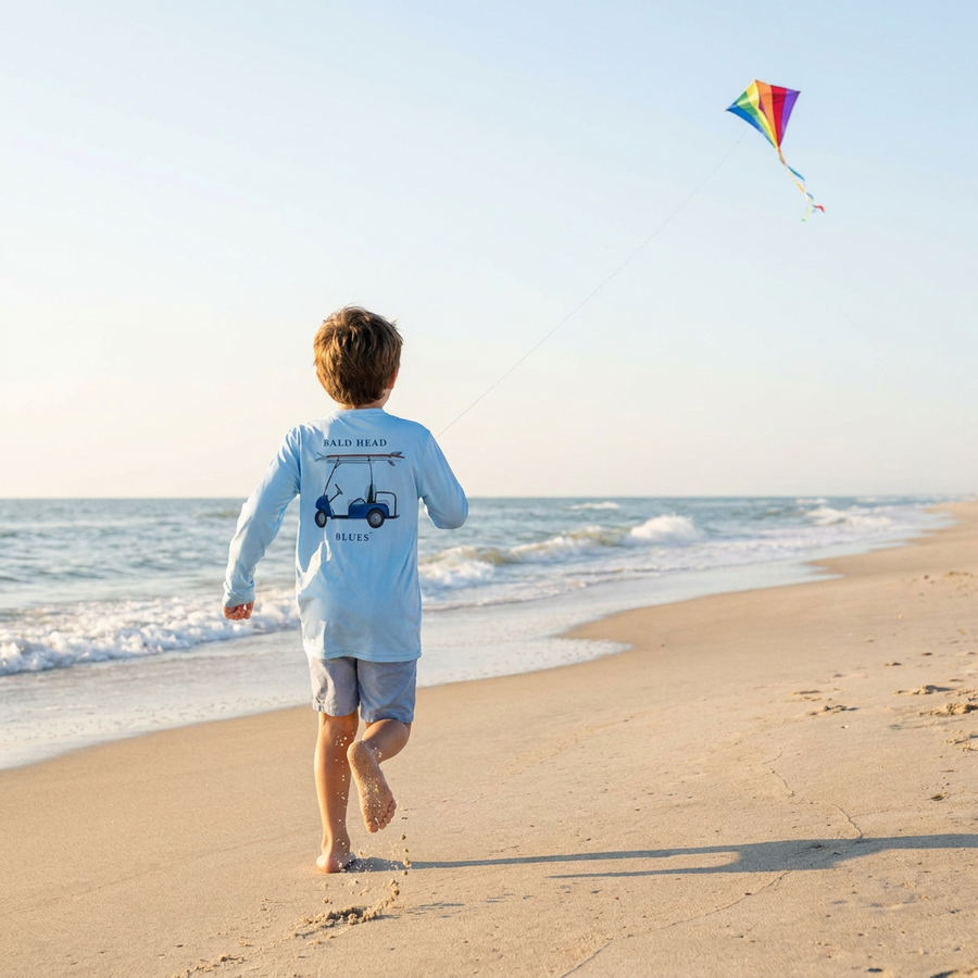 Child running on the beach flying a kite in a blue long-sleeve tee