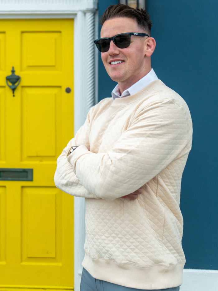 Man in a quilted Cape crew neck in front of a yellow beach-house door