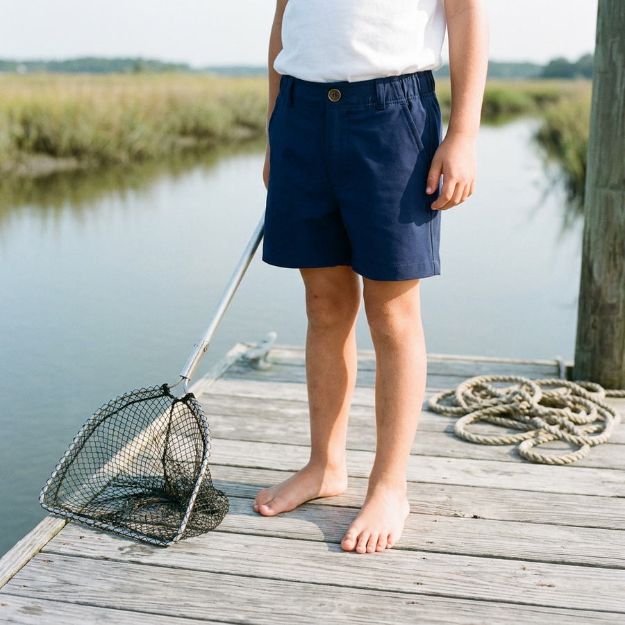 Waist-down view of a child in navy shorts standing on a marsh dock with a crabbing net